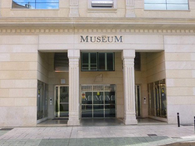 Gro├če Geb├Ąude mit Glasfenstern und -türen, S├Ąulen und Text an der Wand, mit einem Weg, der zur Museums├Ąnterung führt.