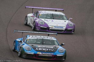 Zwei Autos fahren auf einer Straße außerhalb einer Stadt, mit Text in der linken unteren Ecke.