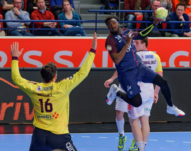 Eine Gruppe von Männern, die auf einem Platz Handball spielen, mit einem Ball in der Luft, in einer Stadionatmosphäre mit Zuschauern und einer Tafel mit der Aufschrift 'Futsal-Weltmeisterschaft 2019 - Paris Saint-Germain vs Bordeaux'.