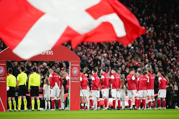 Eine Gruppe von Menschen auf einem Fußballfeld mit einer roten und weißen Flagge im Vordergrund, einem Bogen mit der Aufschrift "Bayern München vs Bayern Munich Betting Tips & Preview" im Hintergrund und einer großen Menge im Stadion.