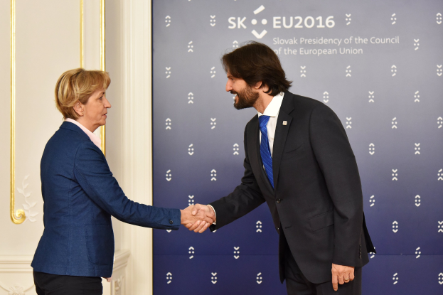 Bundeskanzlerin Angela Merkel und Joachim Gauck schütteln Hände bei einem EU-Gipfeltreffen, lächeln und stehen vor einem Banner und einer Tür.
