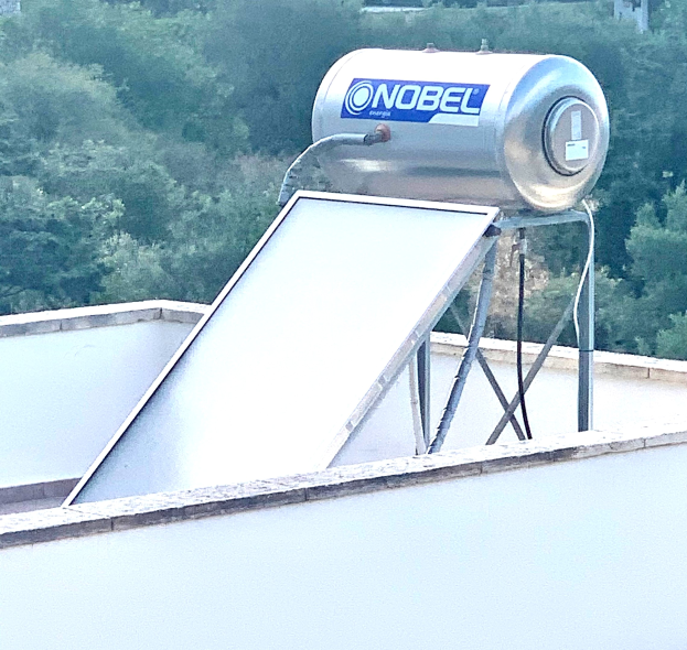 Solarwassererhitzer mit einem Speicherbehälter auf dem Dach eines Gebäudes, vor einem Hintergrund von Bäumen.