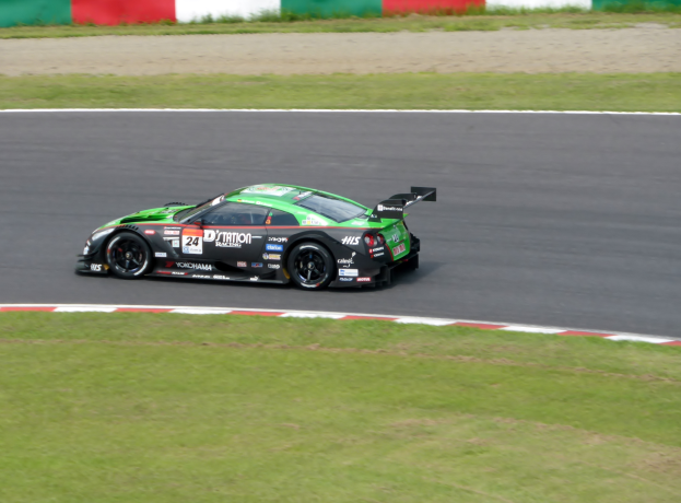 Ein Sportwagen mit Text und Zahlen, der beim 24-Stunden-Rennen von Le Mans teilnimmt, fährt auf einer Rennstrecke mit Gras auf beiden Seiten und einer Wand im Hintergrund.