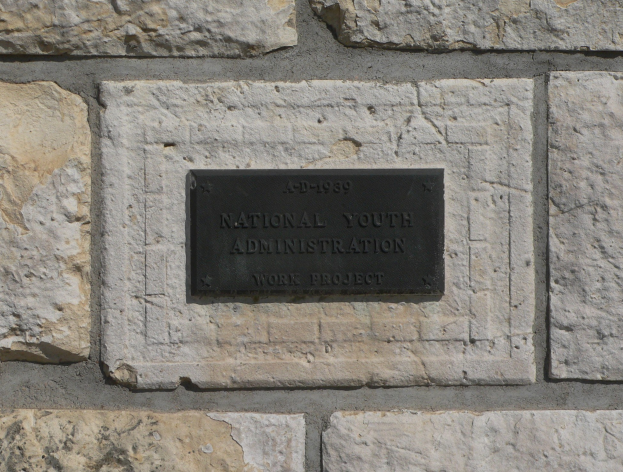 Steinwand mit einem rechteckigen schwarzen Schild, auf dem "Nationaler Jugenddienst" in weißer, fetter, zentrierter Schrift steht.