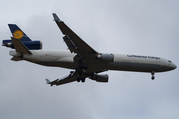 Ein Lufthansa Cargo Boeing 777-300ER im Flug, mit ausgebreiteten Flügeln und laufenden Triebwerken gegen einen bewölkten Himmel mit sichtbarem Text auf dem Rumpf.