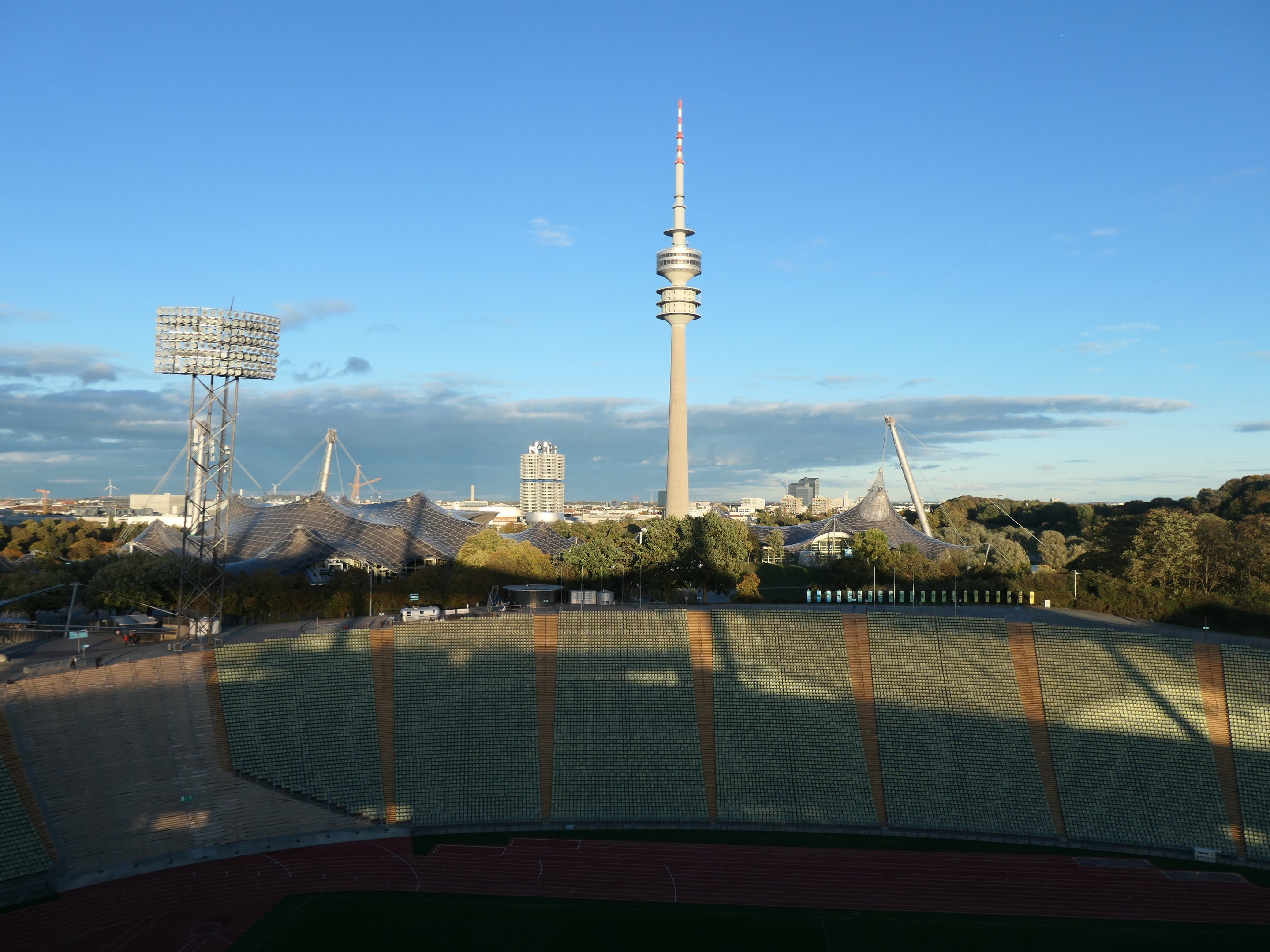 Olympiastadion in Berlin mit dem Fernsehturm im Hintergrund, umgeben von Bäumen, Gebäuden und Lichtern unter einem bewölkten Himmel.