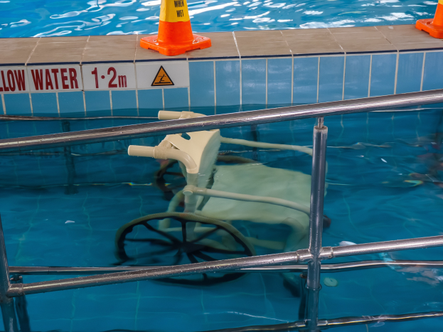 Schwimmbad mit einem Stuhl in der Mitte, umgeben von Sicherheitskegeln und einem Geländer sowie einem Schild an der Wand, das verfügbare Schwimmausrüstung anzeigt.