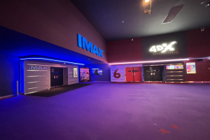 Innenseite eines Kinos mit einem violetten Teppich, Text und Bildschirme an den Wänden und Deckenleuchten.