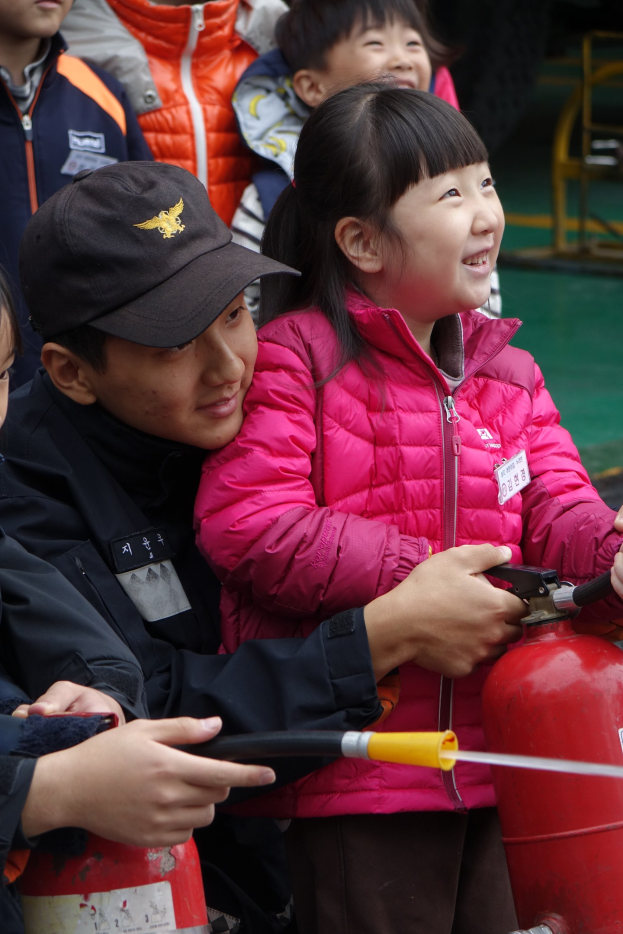 Gruppe von Kindern um ein rotes Feuerhydrant in einer Schulumgebung, eines Kindes hält ein Rohr.