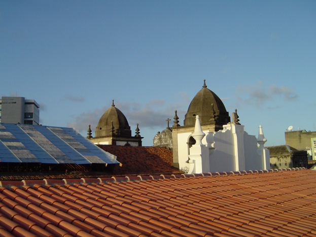 Eine Stadtansicht mit mehreren Gebäuden im Vordergrund unter einem blauen Himmel, mit Solarpanelen auf dem Dach eines Gebäudes.