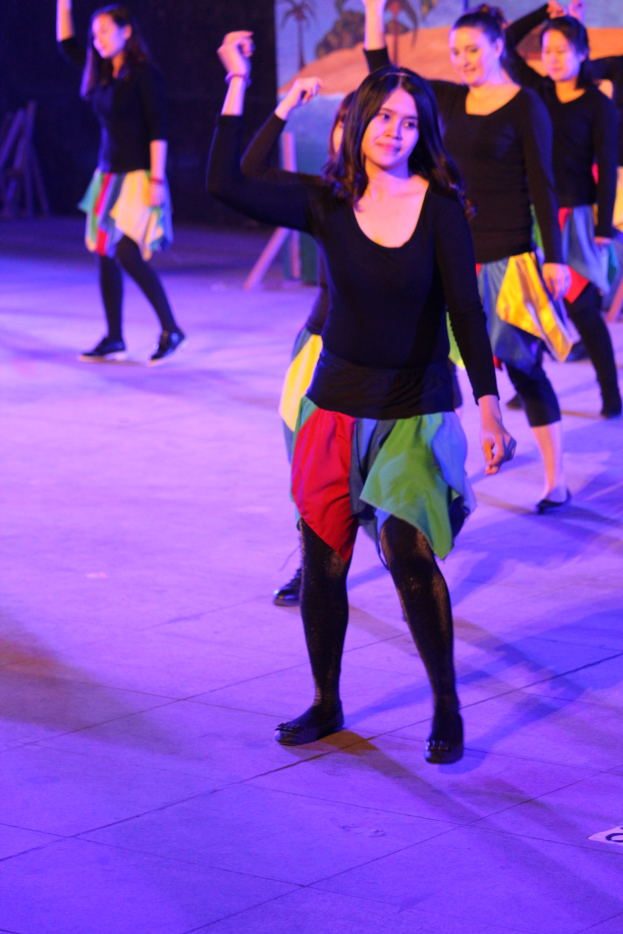 Gruppe junger Frauen, die auf einer Bühne tanzen, mit einem Gemälde im Hintergrund.