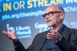 Steve Ballmer, ein Mann im Anzug und mit Brille, spricht in ein Mikrofon mit einem Hintergrundbild.