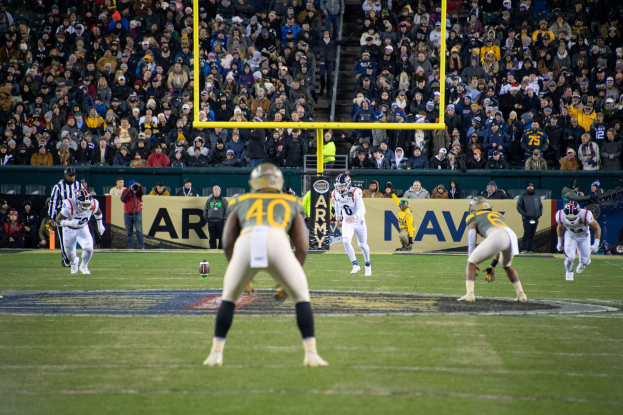 Fußballspieler in Helmen und Uniformen konkurrieren auf einem Feld mit Zuschauern in den Rängen und sichtbaren Stadionwerbung.