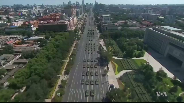 Luftaufnahme einer Stadtstraße mit fahrenden Autos, flankiert von Bäumen und Gebäuden, unter einem sichtbaren Himmel, mit einem Wasserzeichen in der rechten unteren Ecke.