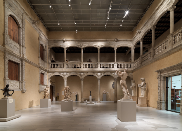 Eine große Museumsgalerie mit zahlreichen Statuen und Skulpturen auf Sockeln, mit architektonischen Elementen wie Wänden, Säulen, Geländern und Deckenleuchten sowie einigen Besuchern.