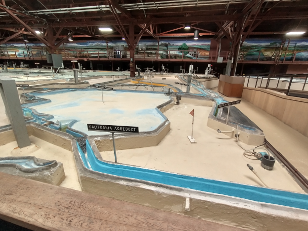 Ein großer Indoor-Wasserpark mit zahlreichen Wasserrutschen, Pfosten, Texttafeln, Deckenleuchten und Wandgemälden, der einem Minigolfplatz ähnelt.
