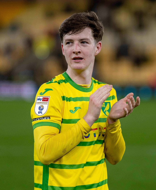 Ein junger Mann in einem gelb-grünen T-Shirt klatscht auf einem Fußballfeld in die Hände, mit einem unscharfen Hintergrund.