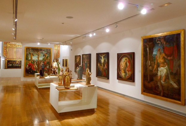 Ein großer Raum im Metropolitan Museum of Art in New York City mit zahlreichen Gemälden an den Wänden, Skulpturen auf Tischen und Deckenleuchten.