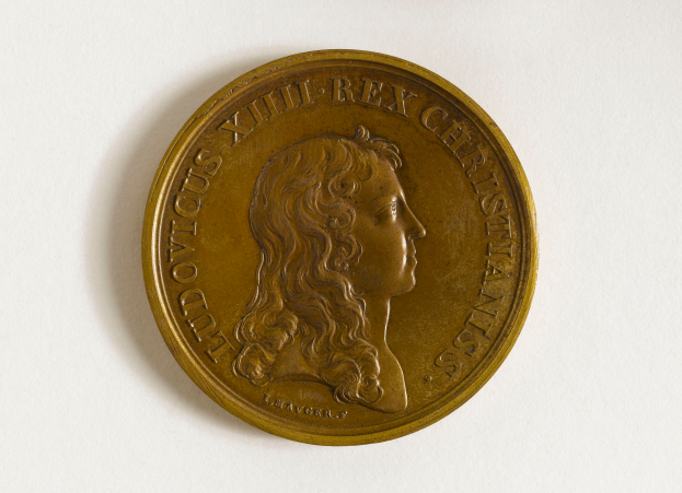 Eine Goldmedaille mit dem Bild einer Frau und der Inschrift "Medaille" darauf, vor einem weißen Hintergrund.