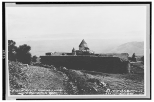 Ein Schwarz-Weiß-Foto eines Klosters umgeben von Bäumen, Hügeln und einem klaren Himmel mit Text unten.