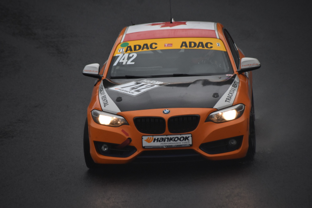 Ein oranger BMW-Rennwagen mit Text und Zahlen auf seiner Karosserie, der auf einer Rennstrecke fährt.