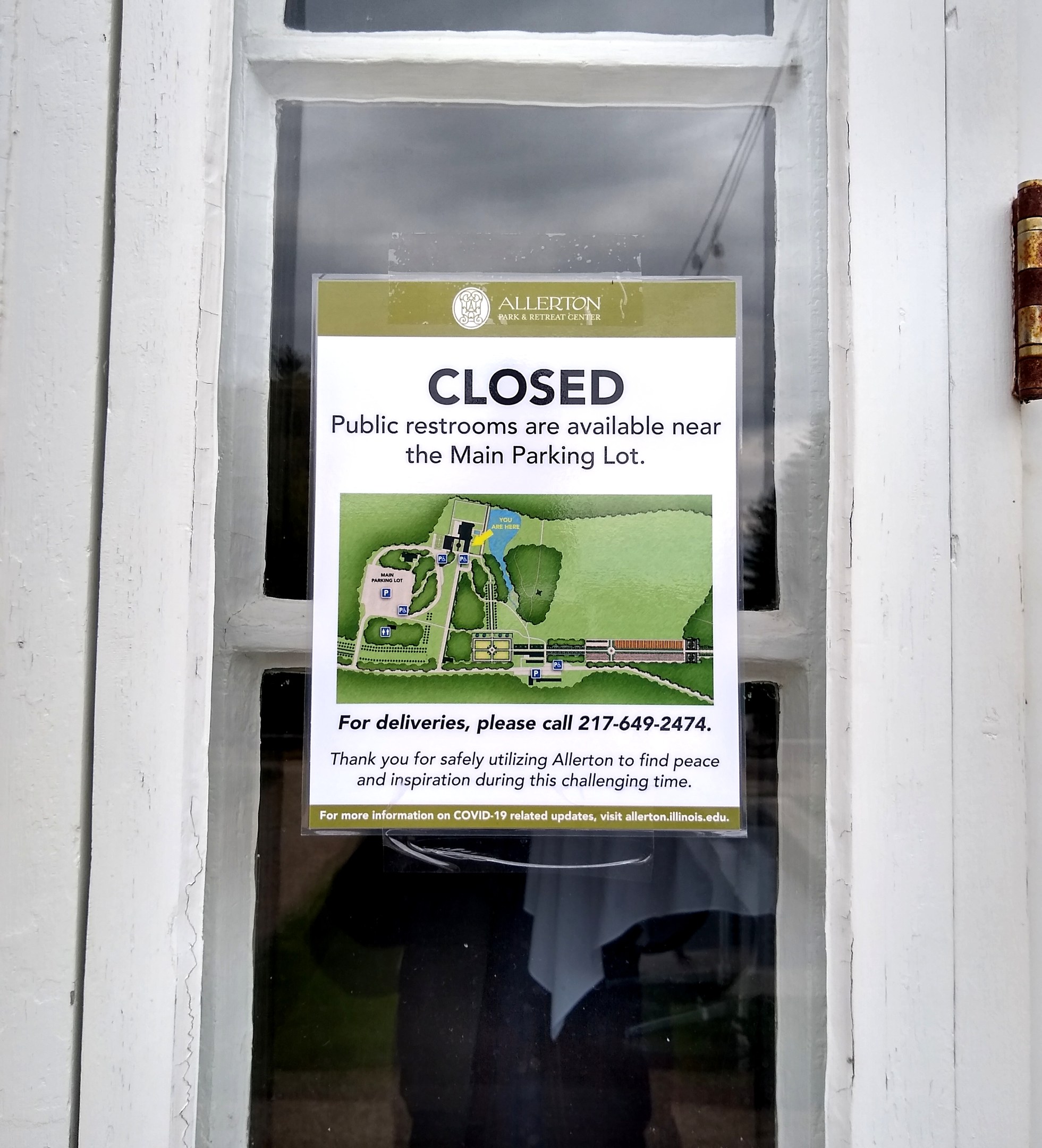 Glasstür mit einem Schild "Geschlossene öffentliche Toiletten in der Nähe des Hauptparkplatzes" und einem unklaren Objekt auf der rechten Seite.