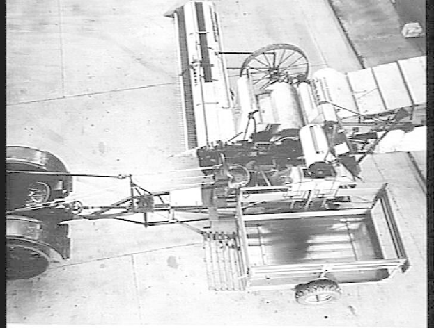 Altes Schwarz-Weiß-Foto eines Lastwagens mit angehängtem Radanhänger, der auf dem Boden geparkt ist, mit Text unten.