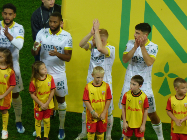 Eine Gruppe junger Fußballspieler in Uniformen klatscht feiernd auf einem Fußballfeld mit einem "Ligue 1"-Schild im Hintergrund.