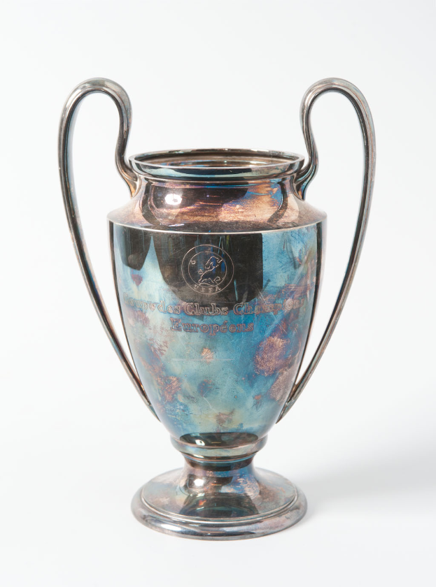 Der UEFA-Champions-League-Pokal, eine stählerne Trophäe mit zwei Griffen und einem blauen und silbernen Farbschema, mit der Inschrift "UEFA Champions League" auf einem weißen Hintergrund.