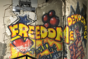 Eine Wand mit Graffiti, das in großen schwarzen Buchstaben "Freiheit und Demokratie" lautet, ein Geländer unten und ein Gebäude mit Fenstern im Hintergrund.