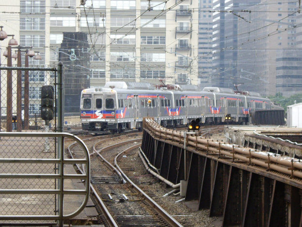 Nahverkehrszug fährt neben Hochhäusern auf erhöhten Gleisen mit sichtbarer Bahninfrastruktur und städtischen Elementen im Hintergrund.