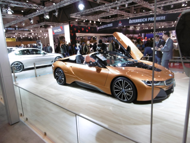 Ein schwarzer BMW i8 Roadster mit Chromakzenten auf der Frankfurt Motor Show umgeben von formell gekleideten G├Ąsten in einer Atmosph├Ąre der Aufregung.