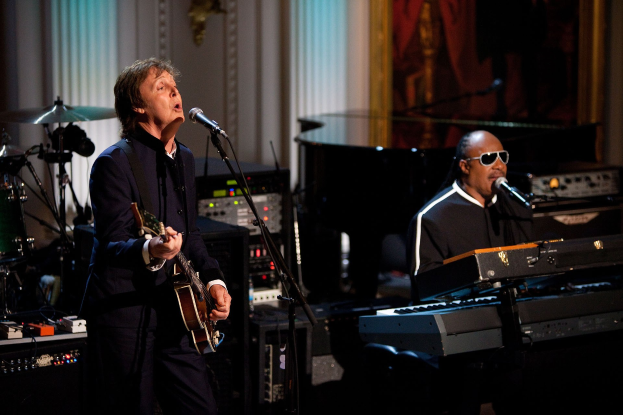 Paul McCartney spielt Gitarre und singt in ein Mikrofon, während Stevie Wonder, der eine Brille trägt, am Piano auf der Bühne der Grammys spielt.