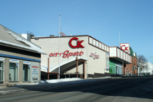 Ein Sportgeschäft in einer Stadt, das an einer Straßenecke liegt und von Gebäuden, Laternen, Bäumen und Schnee umgeben ist, mit dem Himmel im Hintergrund.
