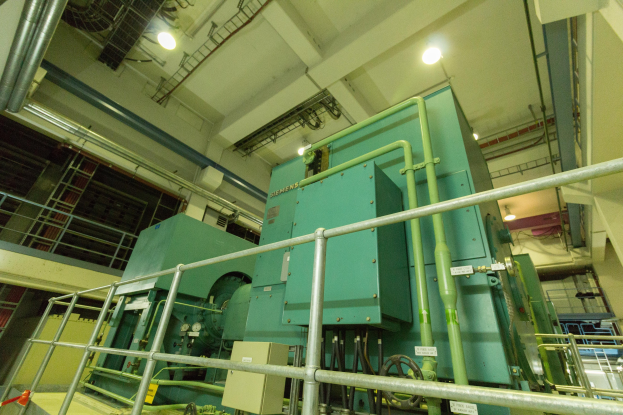 Großer industrieller Wärmetauscher in einem Gebäude, umgeben von Geländern, Rohren, Ventilen und Beleuchtungsinfrastruktur.