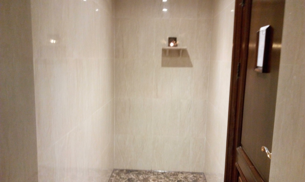 Ein Badezimmer mit einer Duschkabine neben einem WC, mit Fliesenwänden, Deckenleuchten und einer Tür auf der rechten Seite.