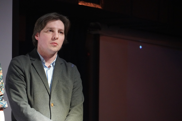 Zwei Personen, ein Mann im Anzug und eine Frau, stehen nebeneinander auf einer Bühne und sehen ernst aus.