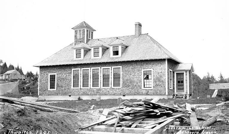 Schwarz-weiß-Foto eines Regierungsgebäudes aus dem Jahr 1905, umgeben von Bäumen unter einem klaren Himmel, mit Holzplanken und dem Text "Regierungsgebäude, Thwaites, 1905" unten.
