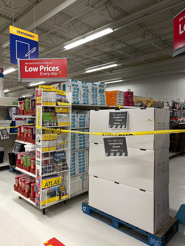 Store interior with stacked boxes, floor signs, clothing racks, informational boards, ceiling lights, and a back wall, marked closed due to the coronavirus pandemic.