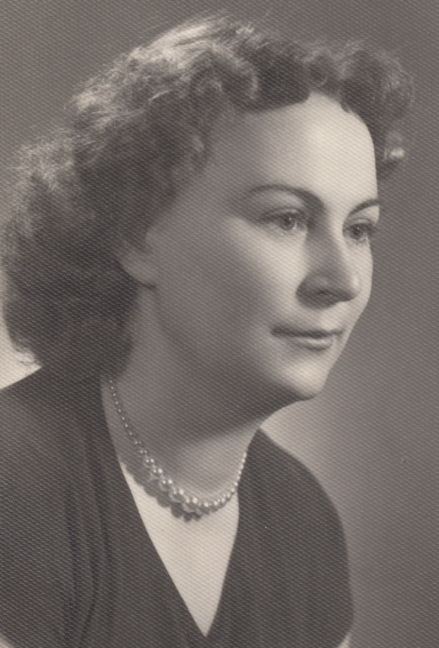 Ein Schwarz-Weiß-Foto einer Frau mit ernstem Gesichtsausdruck, die eine Kette trägt und ein einfaches Kleid mit hohem Kragen und langen Ärmeln trägt, mit zurückgebundenem Haar.