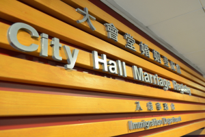 Ein hölzernes Schild an einem Gebäude trägt die Aufschrift "Stadthaus Standesamt" mit zusätzlichem Text darunter, unter einer Decke.