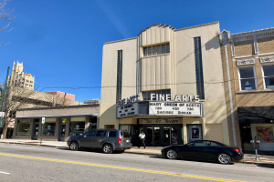 Außenansicht des Feinschmecker-Theaters in St. Louis, Missouri, mit Fahrzeugen auf der Straße, einem Fußgänger auf dem Gehweg, einem Wegweiser, Bäumen, Gebäuden und Himmel im Hintergrund.