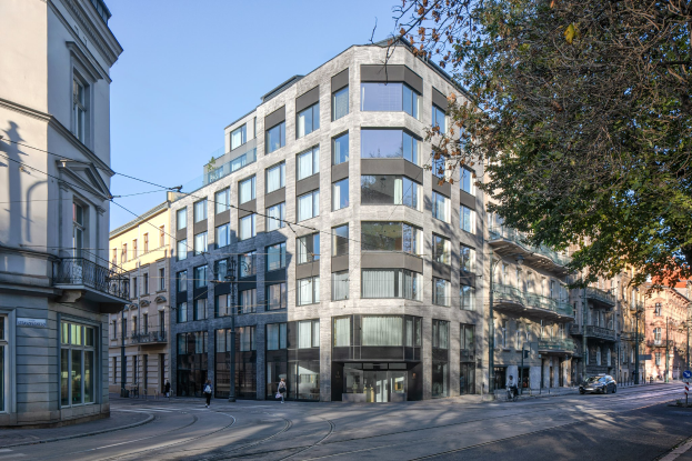 Großes Bürogebäude mit mehreren Fenstern, umgeben von Straßeninfrastruktur, Fahrzeugen, Fußgängern, Bäumen und einem bewölkten Himmel.