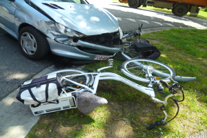 Auto am Straßenrand nach Zusammenstoß mit Fahrrad auf dem Gras liegend, Bäume und klarer blauer Himmel im Hintergrund.