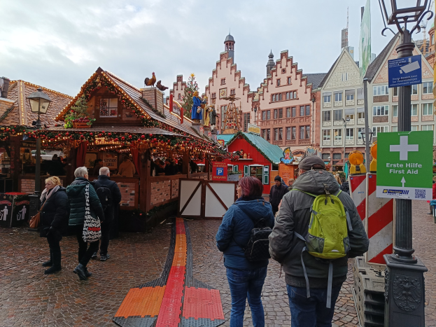 Menschen auf Kopfsteinpflasterstraße neben einem Weihnachtsmarkt in Nürnberg mit Laternen und Texttafeln im Bild.