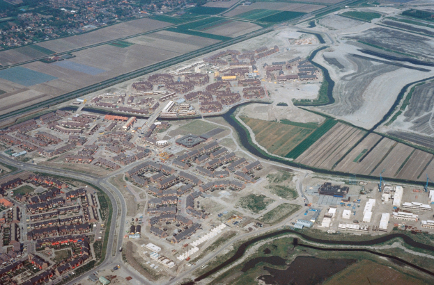 Luftaufnahme einer Stadt mit dichtem Baumbestand, Straßen, Feldern, Bäumen und einem zentralen Reservoir.