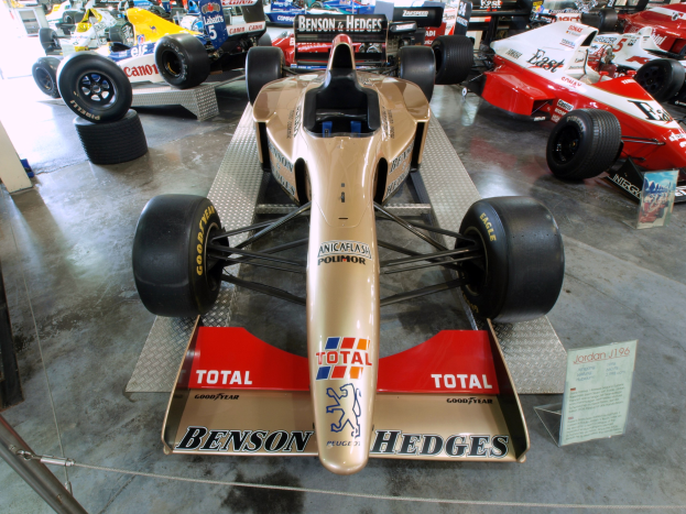 Eine Gruppe von Rennwagen, die in einem Museum hinter einem Metallzaun ausgestellt sind, mit informativem Text im Hintergrund.