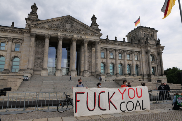 Gruppe von Menschen mit einem "Fuck You Coal"-Schild vor dem Reichstag in Berlin, mit seinen architektonischen Details, einem Fahrrad, Bäumen, einem Fahnenmast und einer bewölkten Himmel.