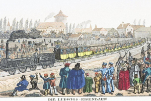 Eine Gruppe von Menschen steht um einen Zug auf den Schienen, einige sitzen im Zug und andere stehen draußen, in der Nähe von Gebäuden und Bäumen, mit dem Text "Ludwigs-Eisenbahn, der erste Bahnhof Deutschlands" unten.