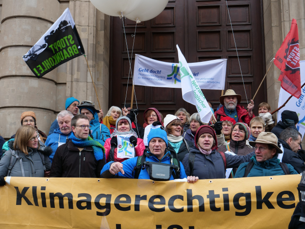 Gruppe von Menschen mit einem Banner, Fahnen und Luftballons vor einem Gebäude mit Säulen während eines Klimastreiks in Deutschland.